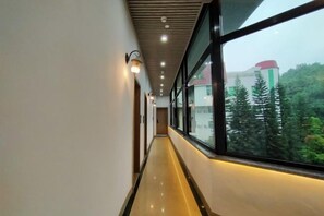 A corridor with a window, ceiling lights, and a view of trees and buildings. - Renhua Shaozhou Impression Boutique Cultural Hotel (Renhua)