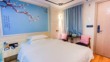 A hotel room with a large bed, a nightstand, a desk, a chair, a wardrobe, and a wall with a decorative painting.