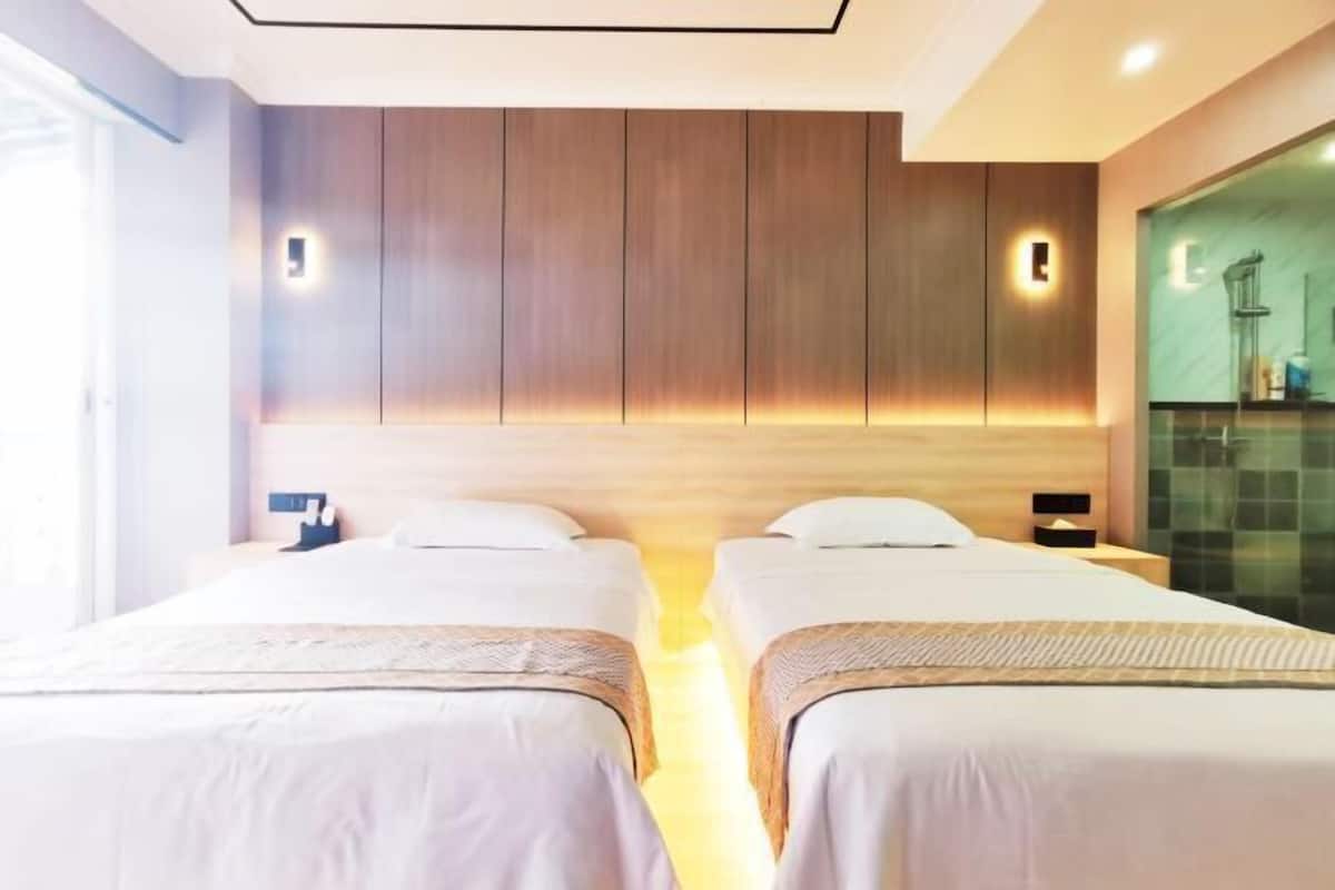 A hotel room with two beds, wooden panel walls, and a glass shower area.