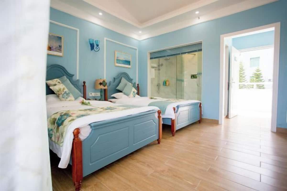 A bedroom with two beds, a glass shower enclosure, and a view of the outdoors.