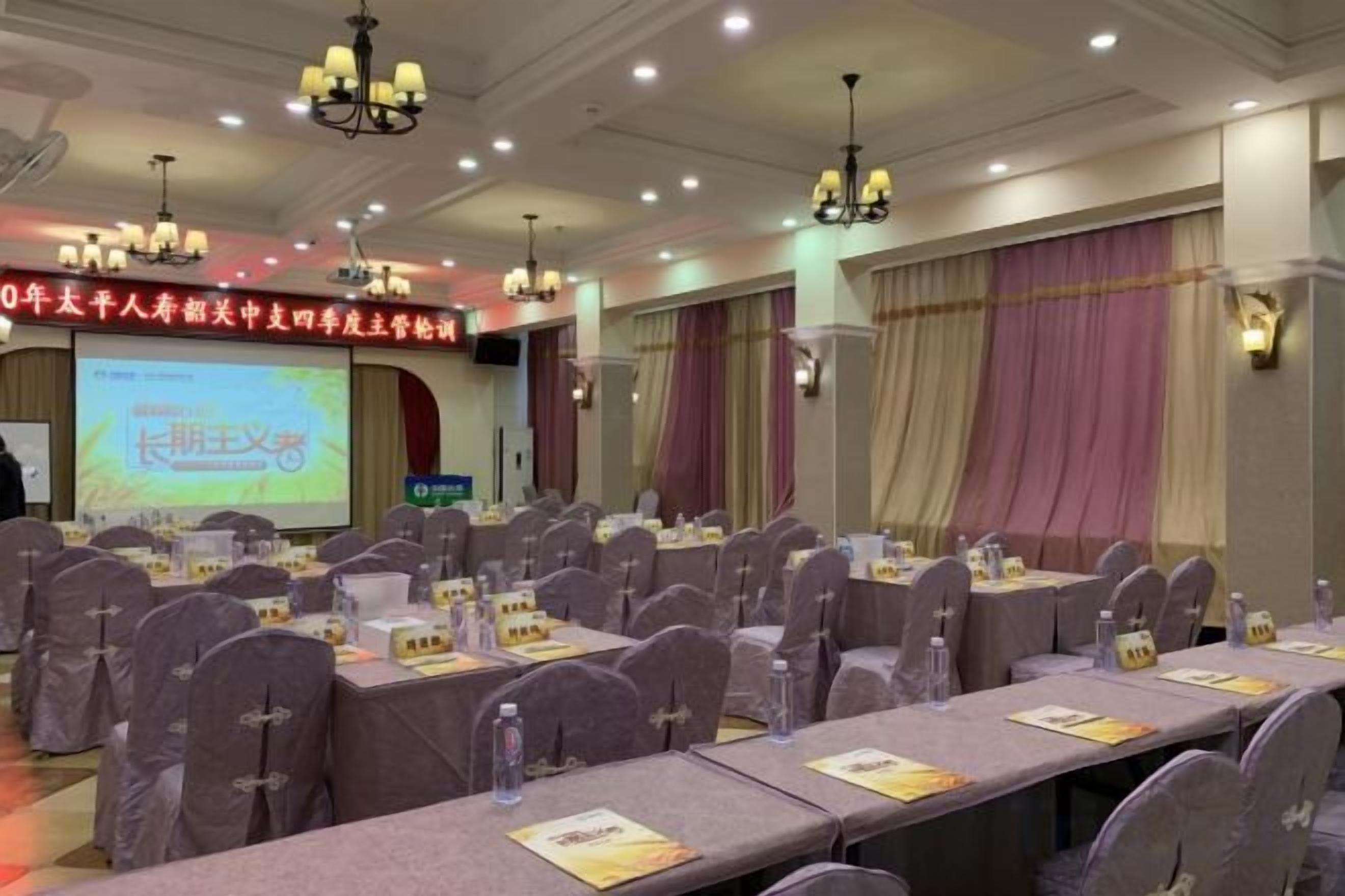 A conference room with rows of tables and chairs, a projection screen, and a banner with text.
