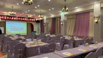A conference room with rows of tables and chairs, a projection screen, and a banner with text.