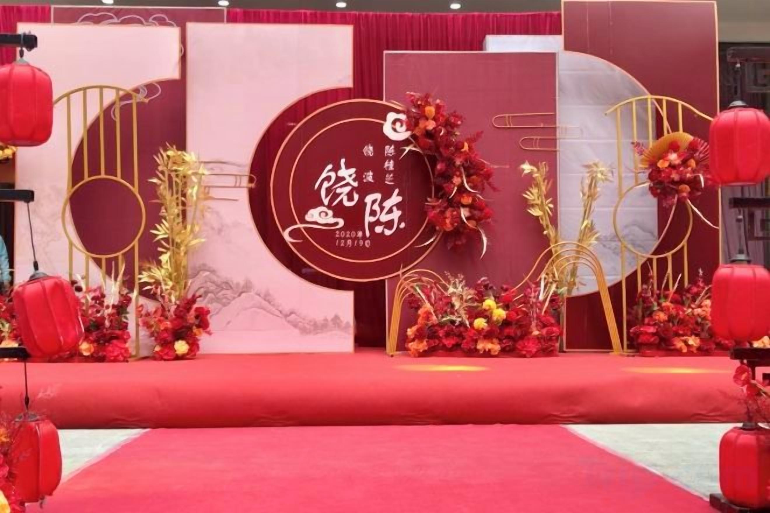 Une scène avec un tapis rouge, des décorations florales et un grand panneau circulaire orné de caractères chinois.