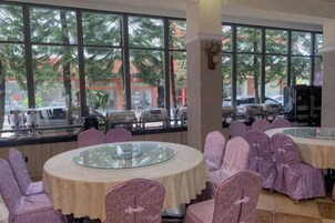 A dining area with round tables and chairs, large windows with a view of palm trees and parked cars.