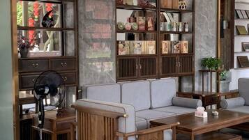 A living room with a sofa, wooden side tables, a fan, and a bookshelf.