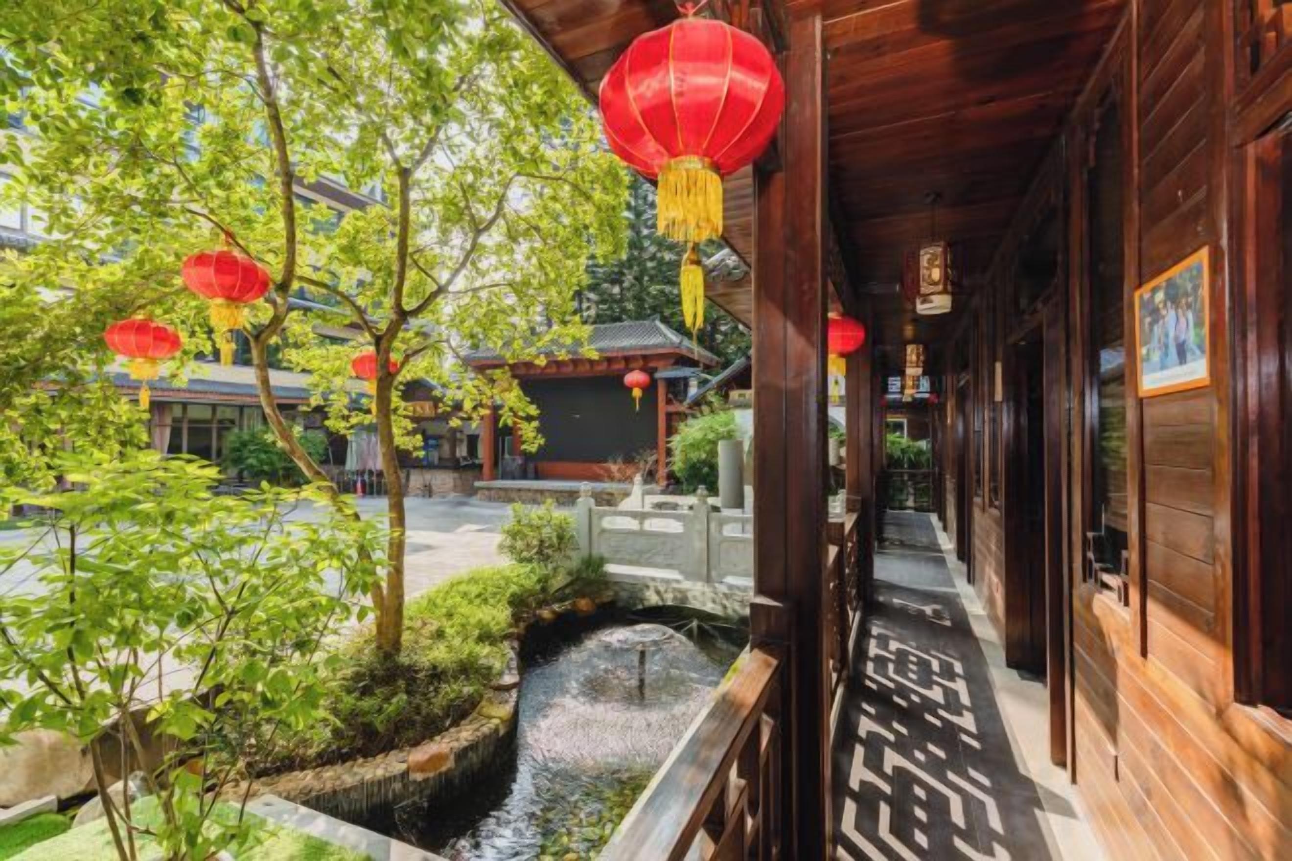 A traditional wooden building with a courtyard, a small water feature, and red lanterns.