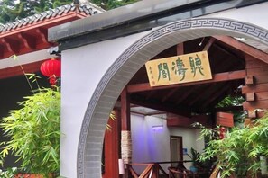 Una entrada de arquitectura china tradicional con un letrero, vigas de madera y plantas en macetas.