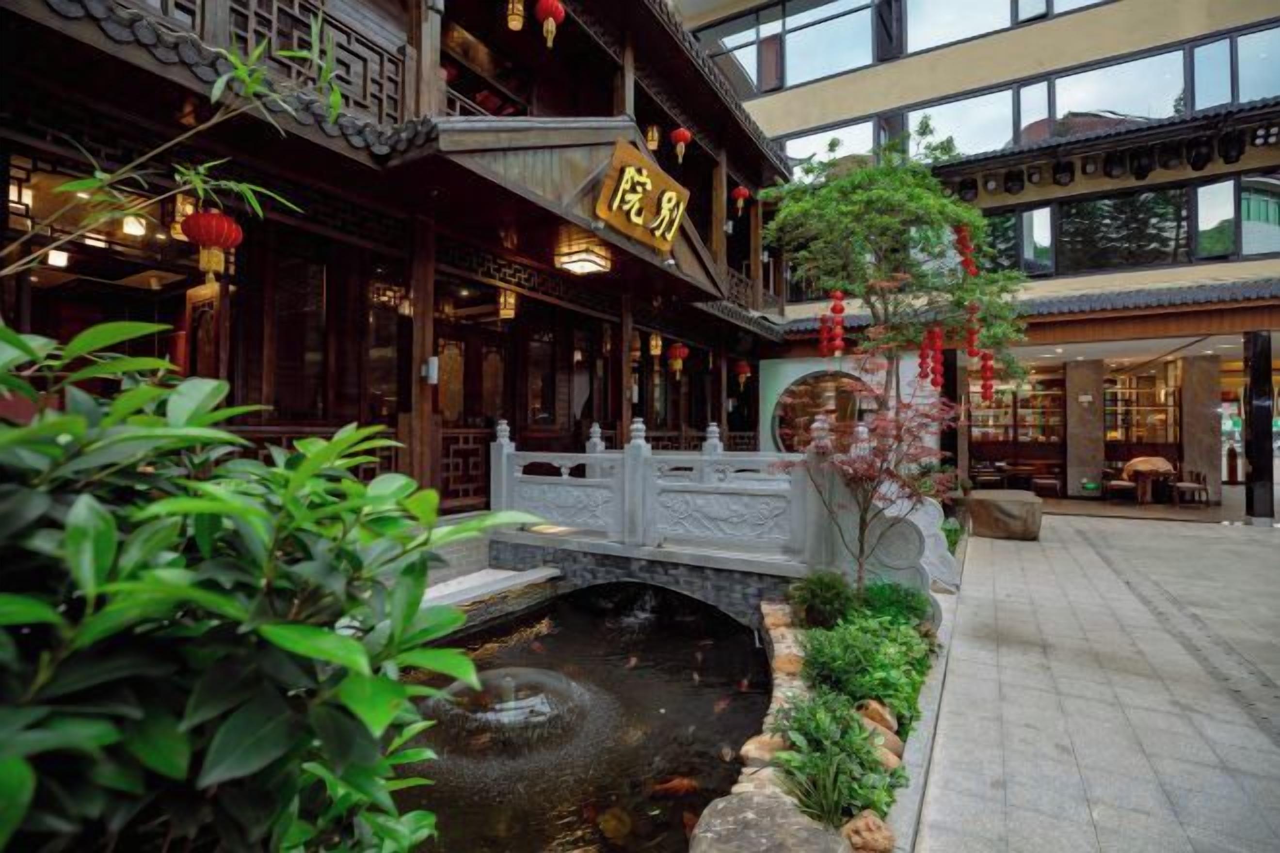 A traditional courtyard with a stone bridge, a koi pond, and a restaurant with a sign.