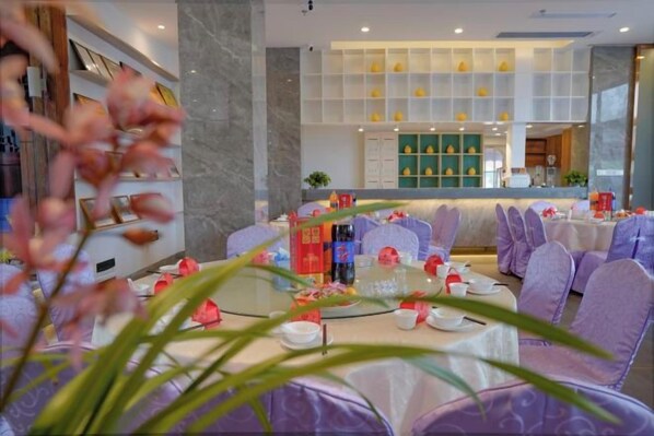 Un restaurante con mesas redondas, sillas moradas y una partición de vidrio.