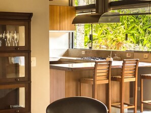 A kitchen with a gas stove, wooden cabinets, and a window with a view of greenery. - Casa térrea com piscina e cozinha de cinema | Granja Viana (Jandira)