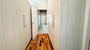 A hallway with wooden flooring and white walls, leading to a room with a window.