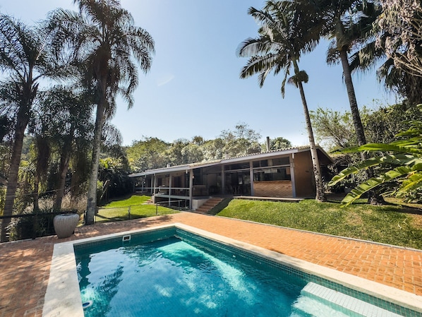 Una casa moderna con piscina, rodeada de palmeras y un césped bien cuidado.