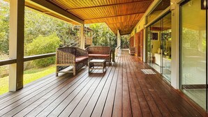 A wooden deck with wicker furniture and glass doors leading to a lush garden. - Casa térrea com piscina e cozinha de cinema | Granja Viana (Jandira)