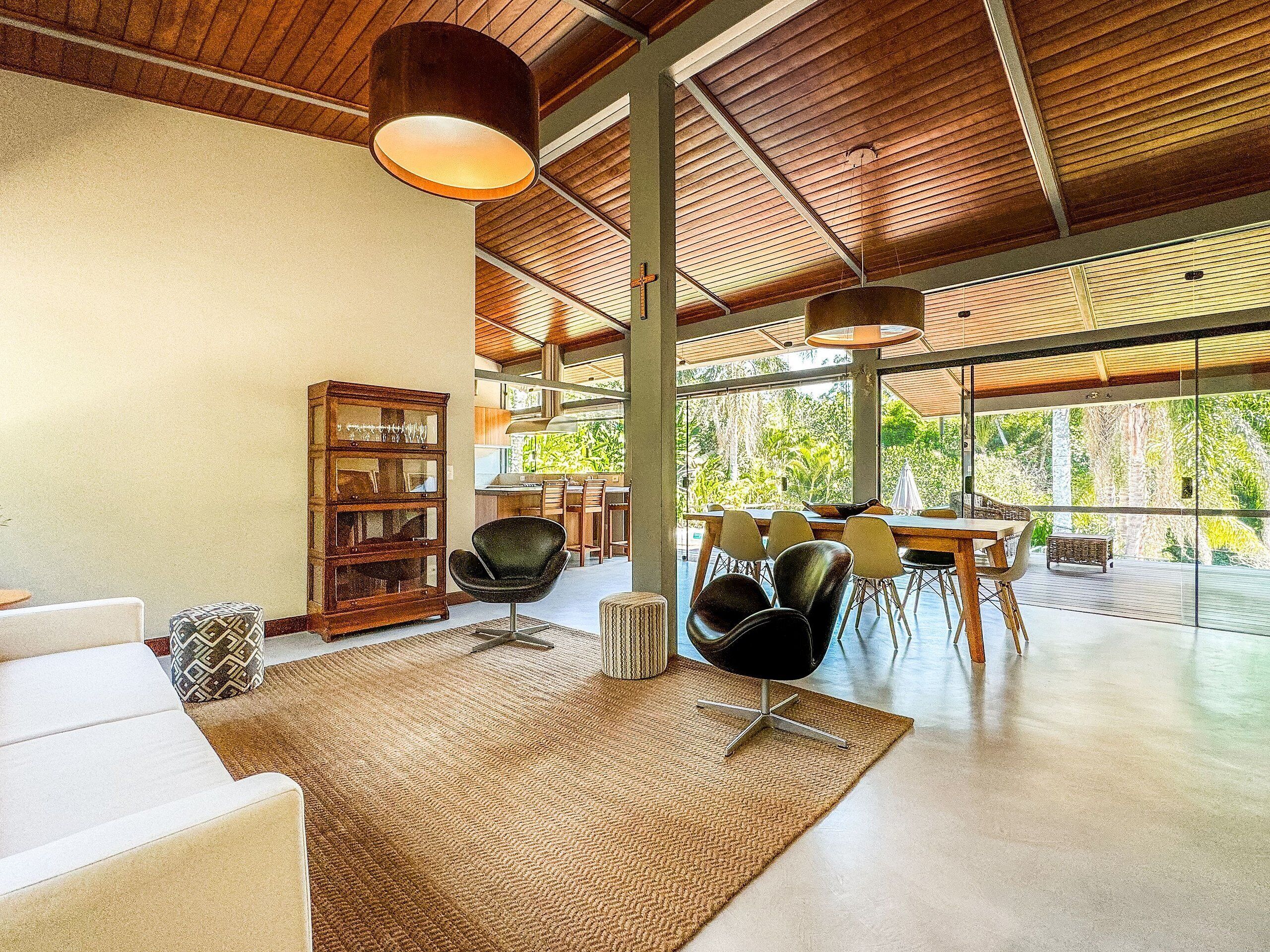 A spacious living area with a large window, a wooden ceiling, and a dining area with chairs and a table.