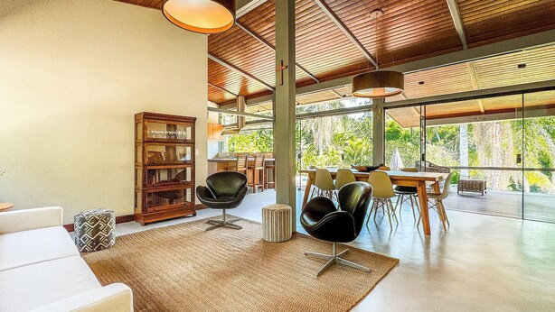 A spacious living area with a large window, a wooden ceiling, and a dining area with chairs and a table.