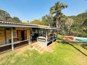 Una casa con patio cubierto, piscina y abundante vegetación.