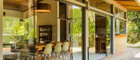 A modern house with a wooden deck, large glass windows, and a dining area with chairs and a table.