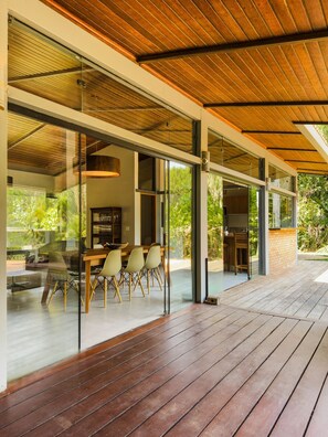 A modern house with a wooden deck, large glass windows, and a dining area with chairs and a table. - Casa térrea com piscina e cozinha de cinema | Granja Viana (Jandira)