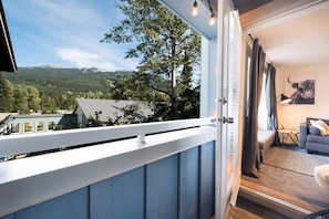 Un balcon avec vue sur les montagnes et les arbres, une balustrade blanche et une pièce comprenant un canapé et une lampe.