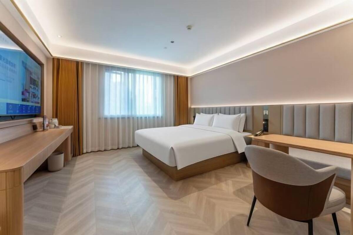 A hotel room with a bed, a desk, a chair, a television, and a window with curtains.