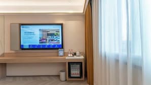 A hotel room with a flat-screen TV mounted on the wall, a small table with a coffee maker, a mini-fridge, and a trash bin. - Starway Hotel (Linhai Intime City) (Linhai)