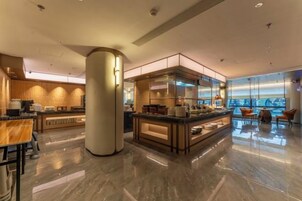 Un moderno vestíbulo de hotel con una barra central, espacios de descanso y vistas amplias a través de grandes ventanales.