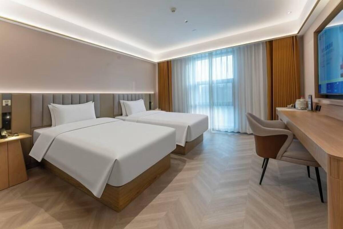 A hotel room with two beds, a desk, and a TV.