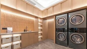 A modern laundry room with wooden cabinets, a sink, and two stacked front-loading washing machines. - Starway Hotel (Linhai Intime City) (Linhai)