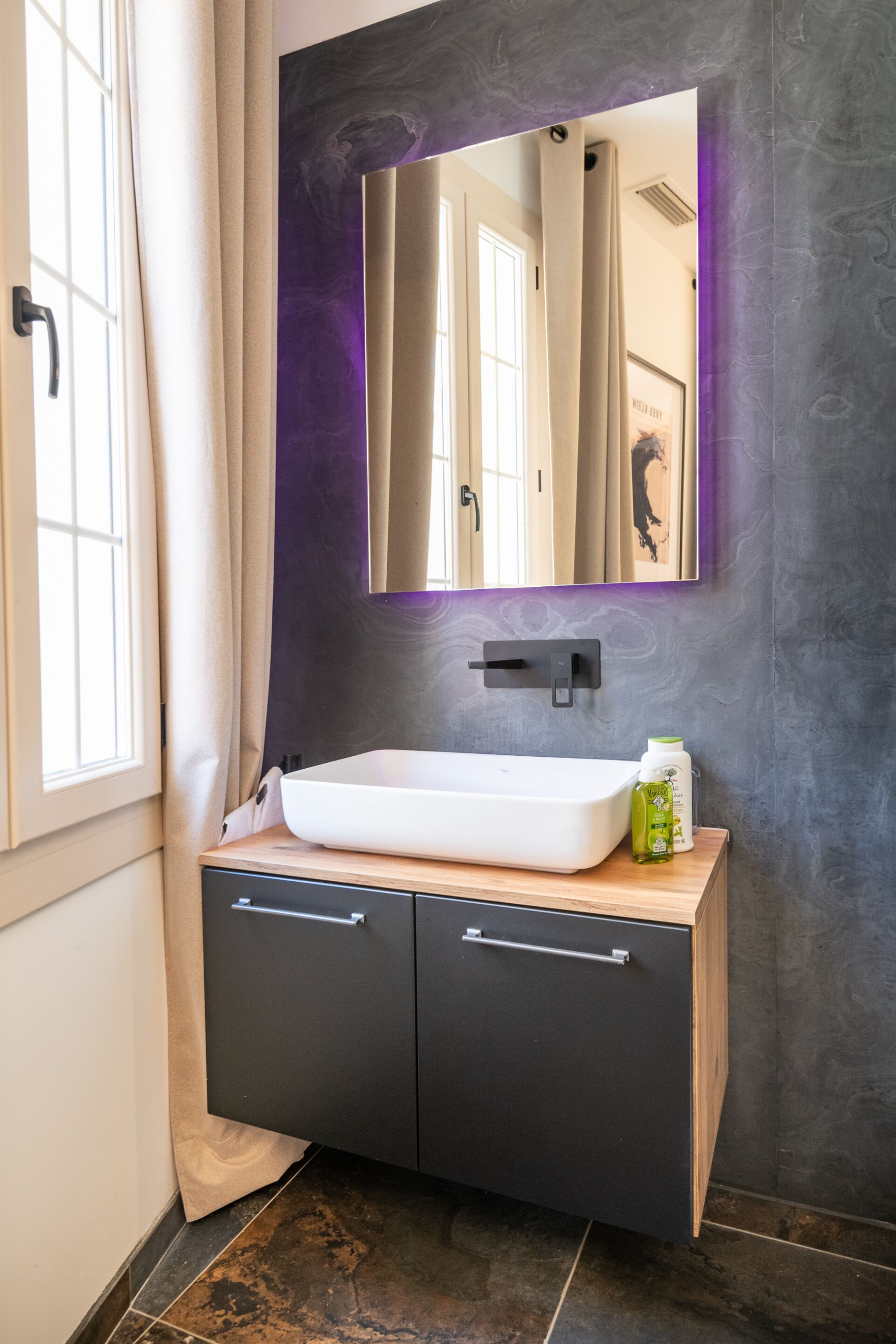Une salle de bain avec un lavabo blanc, des meubles sombres et un miroir doté d’un cadre violet.