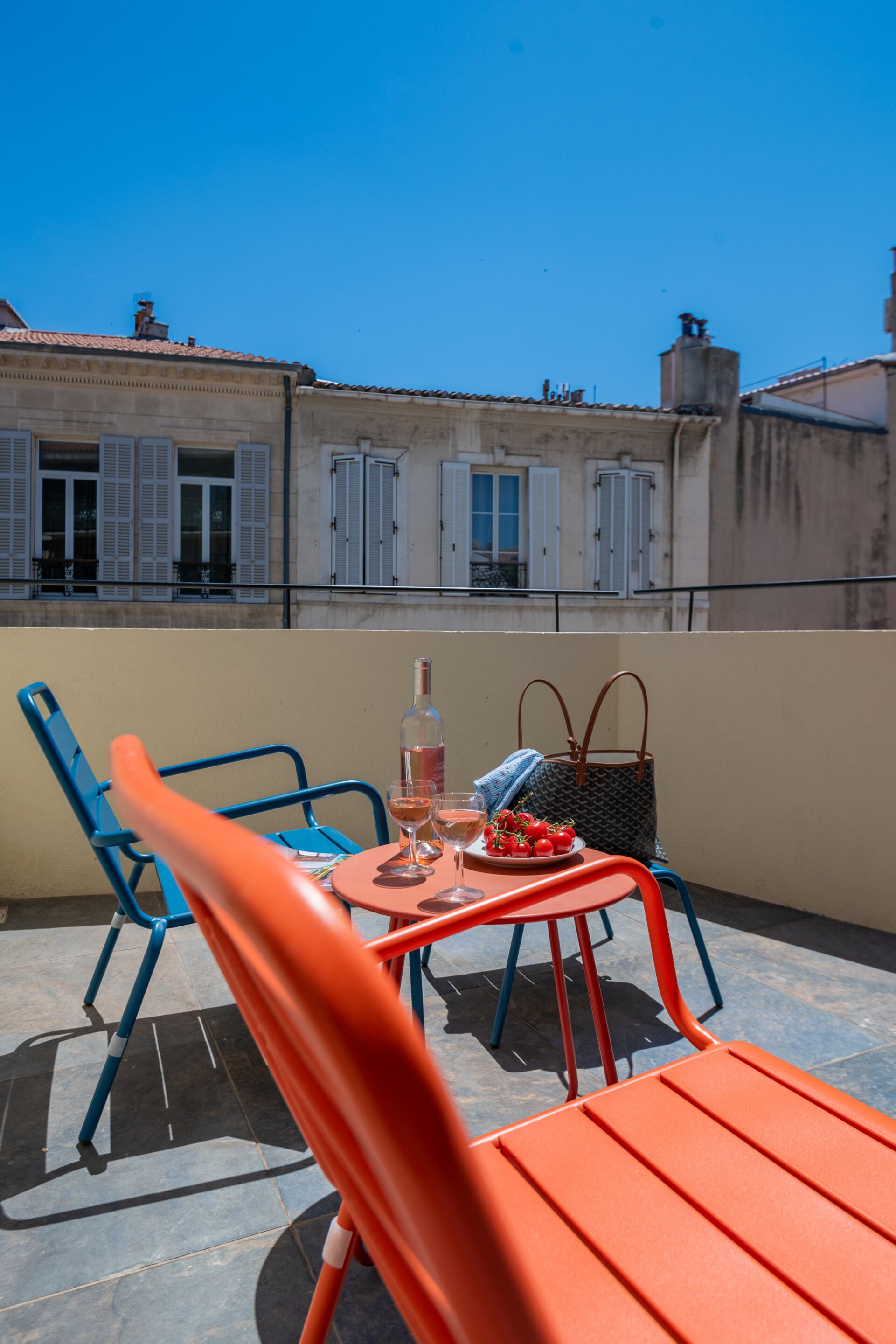 Une terrasse sur le toit avec une table dressée pour deux personnes, agrémentée d’une bouteille et de verres, ainsi que d’une assiette de tomates.