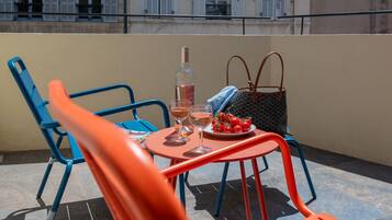 A rooftop terrace with a table set for two, featuring a bottle and glasses, and a plate of tomatoes.