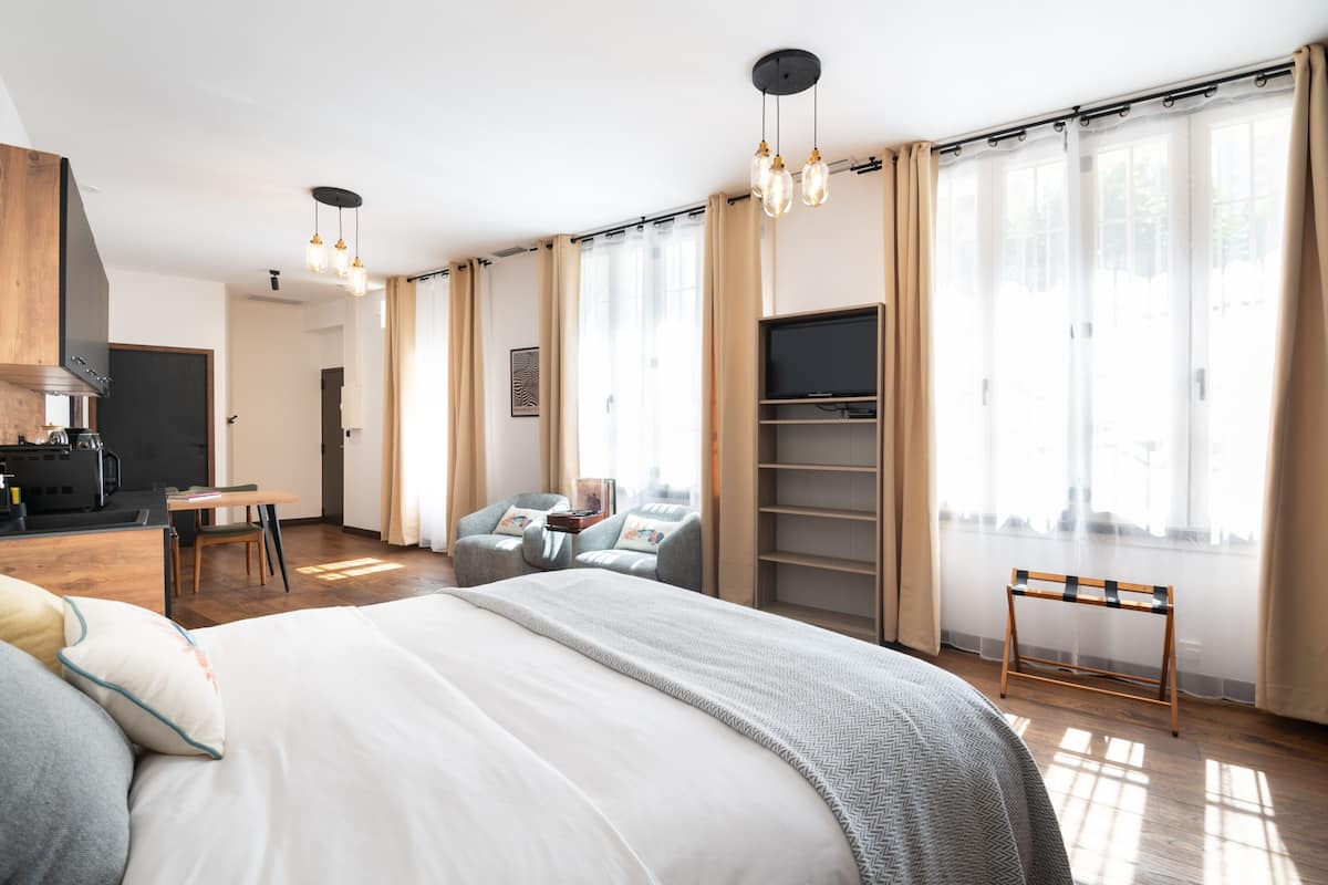 A modern hotel room with a large bed, a desk, a chair, a TV, and a wardrobe.