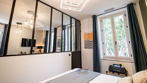 Ein modernes Schlafzimmer mit einem großen Spiegel, einem Bett mit einem Buch, einem Nachttisch und einem Fenster mit Vorhängen.