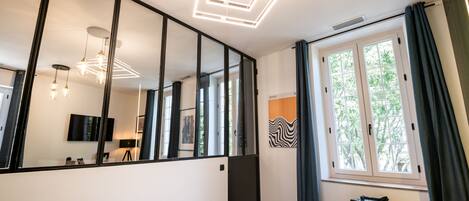A modern bedroom with a large mirror, a bed with a book, a side table, and a window with curtains.