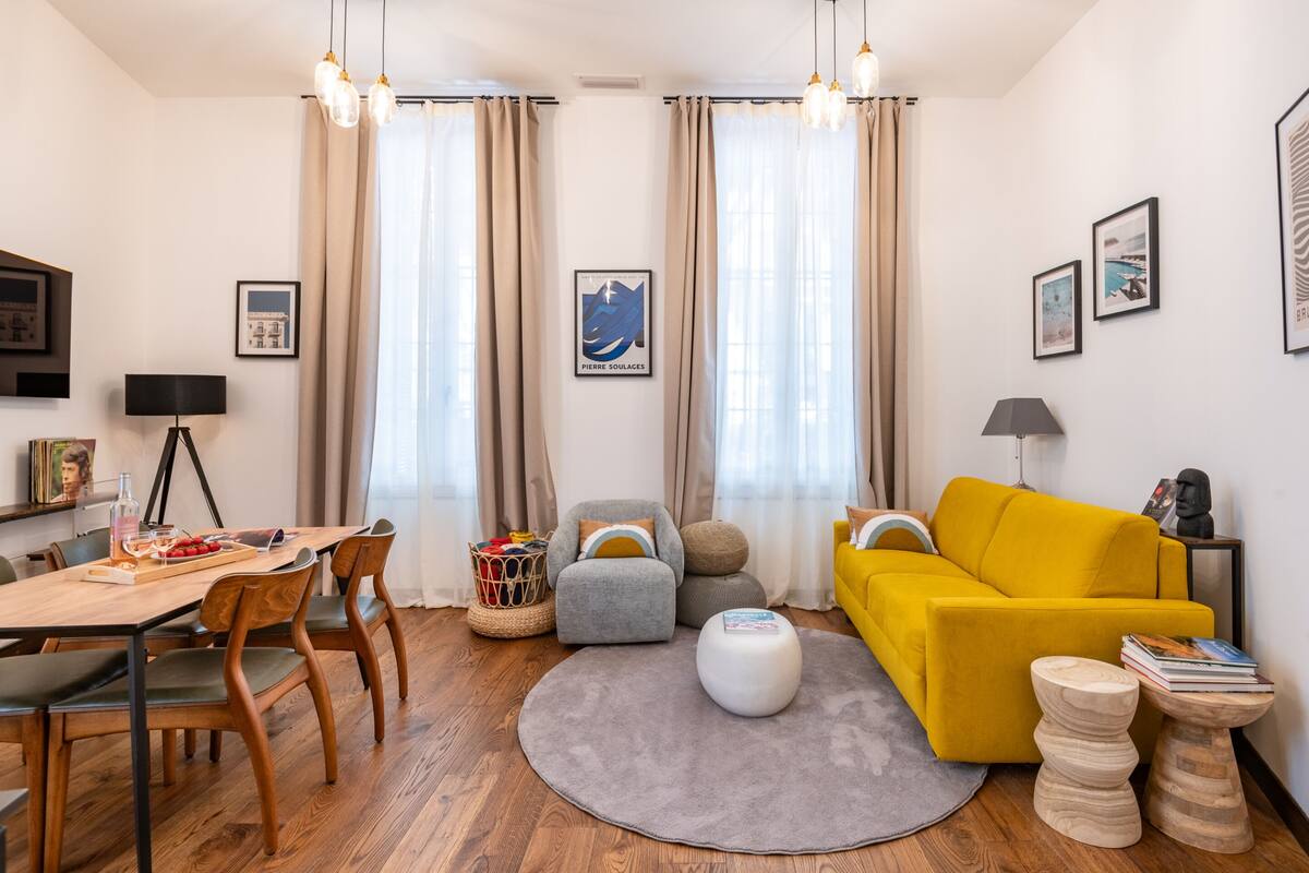 A modern living room with a wooden dining table, a yellow sofa, and a grey rug.