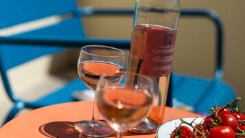 A table with a bottle of wine, two glasses, a plate of cherry tomatoes, and a pair of sunglasses.