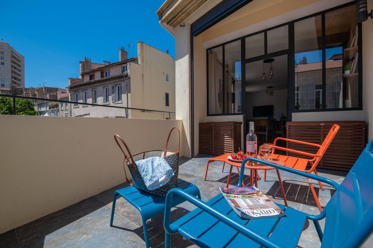 A balcony with blue metal chairs, a table with a bottle and glasses, and a handbag.