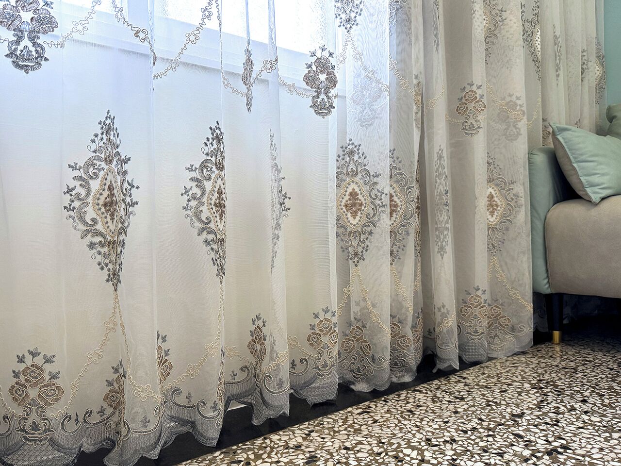 A room with a patterned carpet and a window with sheer curtains featuring floral designs.