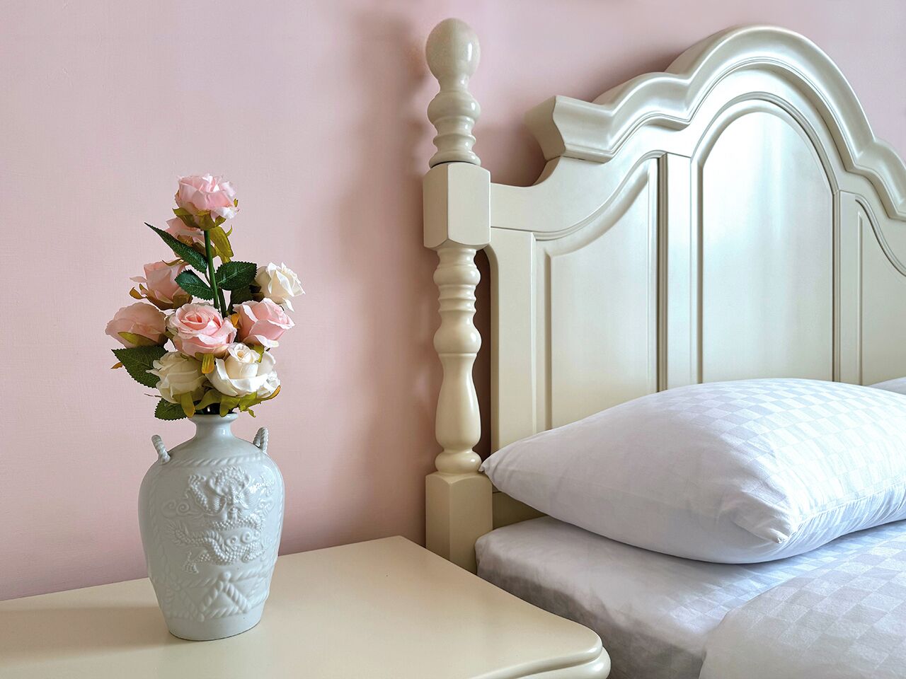 A bedroom with a bed, a nightstand, and a vase with flowers.