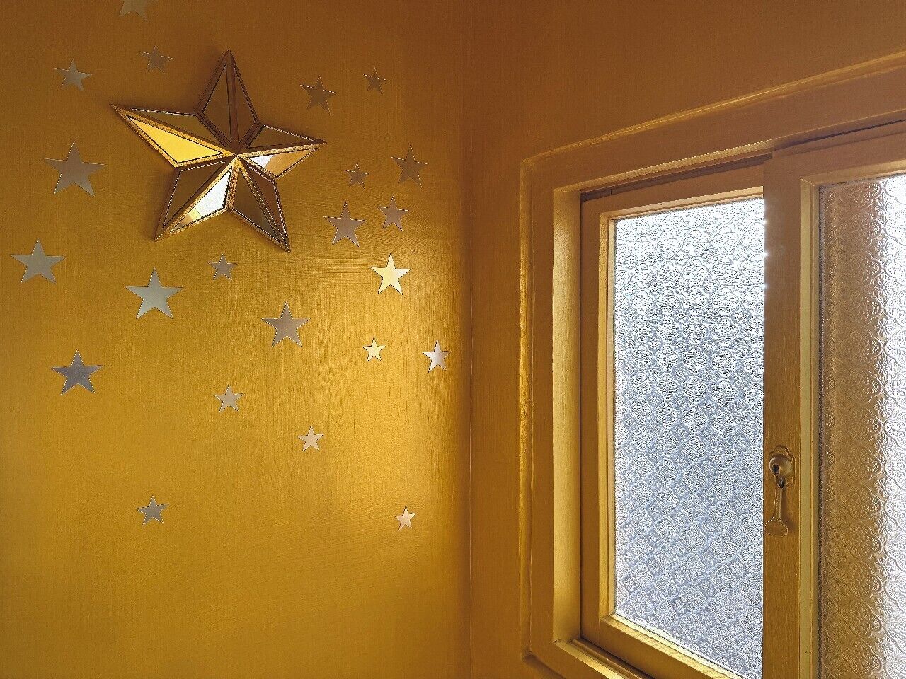 Ein Zimmer mit Fenster, einer Sternenverzierung an der Wand und einer strukturierten Tür.