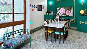 A dining area with a table and chairs, a bench, a green wall, and a window with a view. - Ronchamp Villa (Tainan)