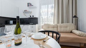 Zona de menjador amb taula preparada per a dues persones, una ampolla de vi i vasos de vi buits. Hi ha un sofà amb coixins estampats al fons.