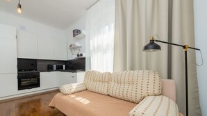 Un apartament modern amb una cuina americana, un sofà amb coixins estampats i una làmpada de peu.