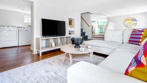 A modern living room with a white sofa, a flat-screen TV, a dining table, and a kitchen area with a washing machine and dryer. - Walk to beach, shuffleboard, and bunk room (Old Orchard Beach)
