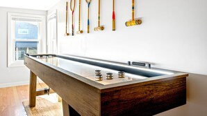 A pool table with a wooden finish and a long rail, a window with blinds, and a wall with various rackets. - Walk to beach, shuffleboard, and bunk room (Old Orchard Beach)