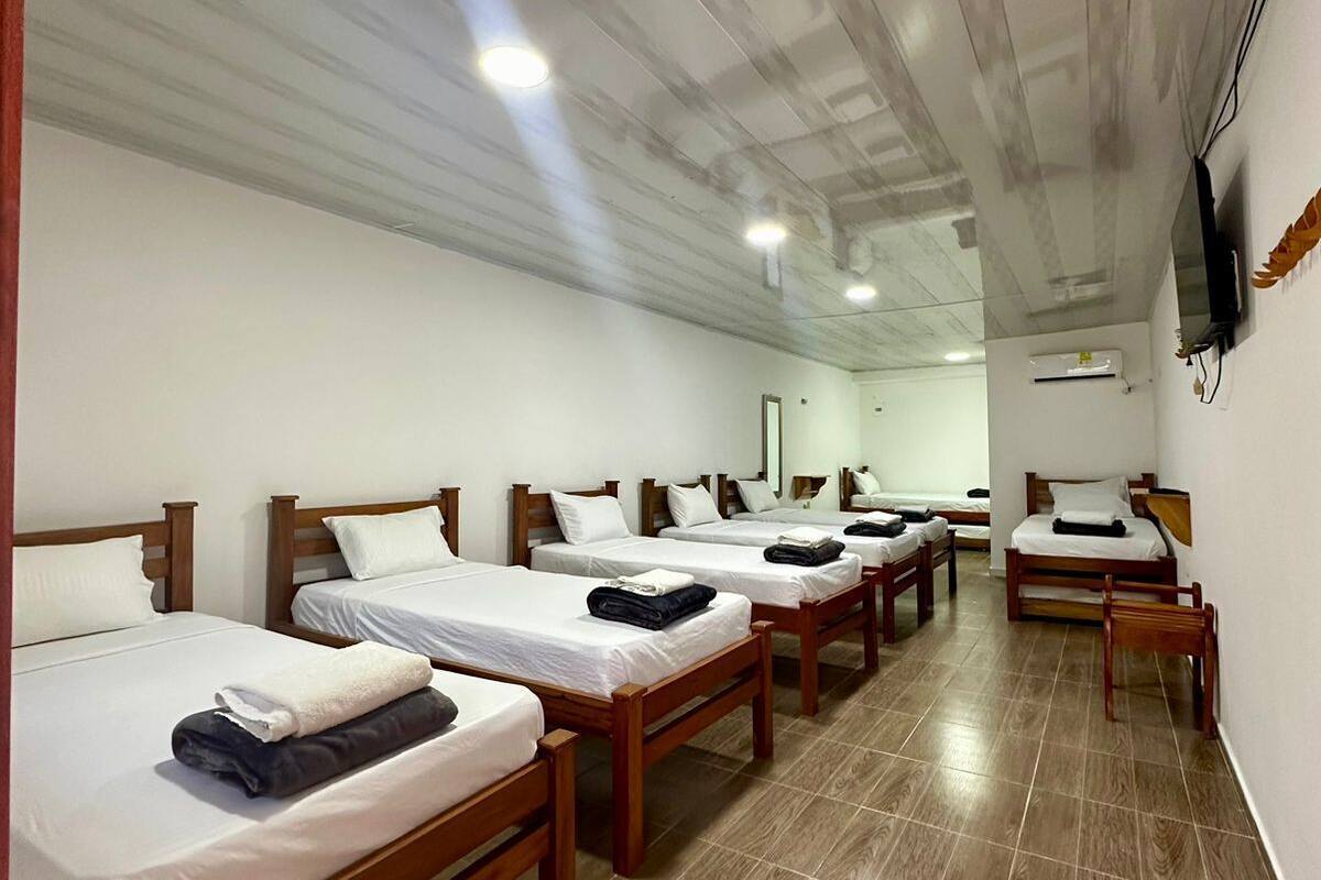 Una habitación de hotel con varias camas de madera, ropa de cama blanca y suelo de baldosas.