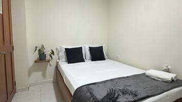 A bedroom with a bed, a potted plant, and an air conditioning unit.