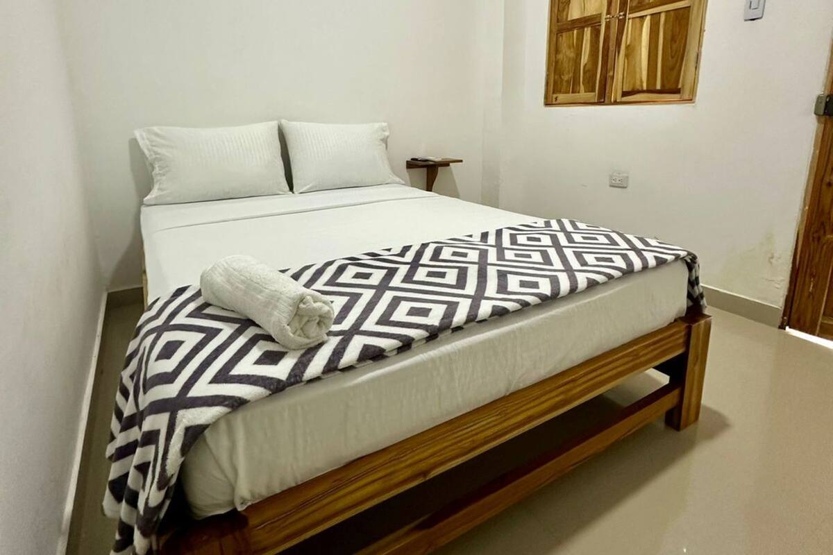 Un dormitorio con cabecera de cama de madera, ropa de cama blanca y una manta de estampado geométrico.