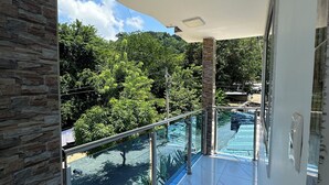 Ein Balkon mit Glasgeländer, ein Pool und Blick auf Grünflächen und einen Berg.