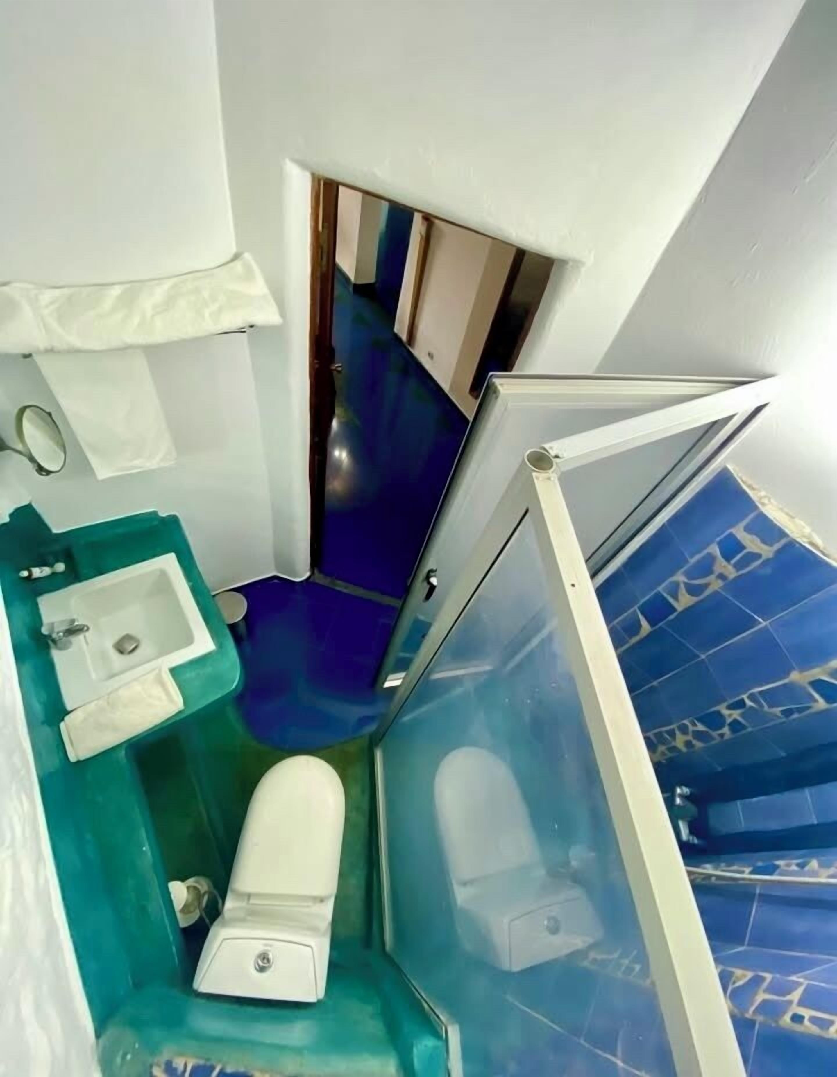 A narrow, angled bathroom with a white sink, toilet, and a small mirror.